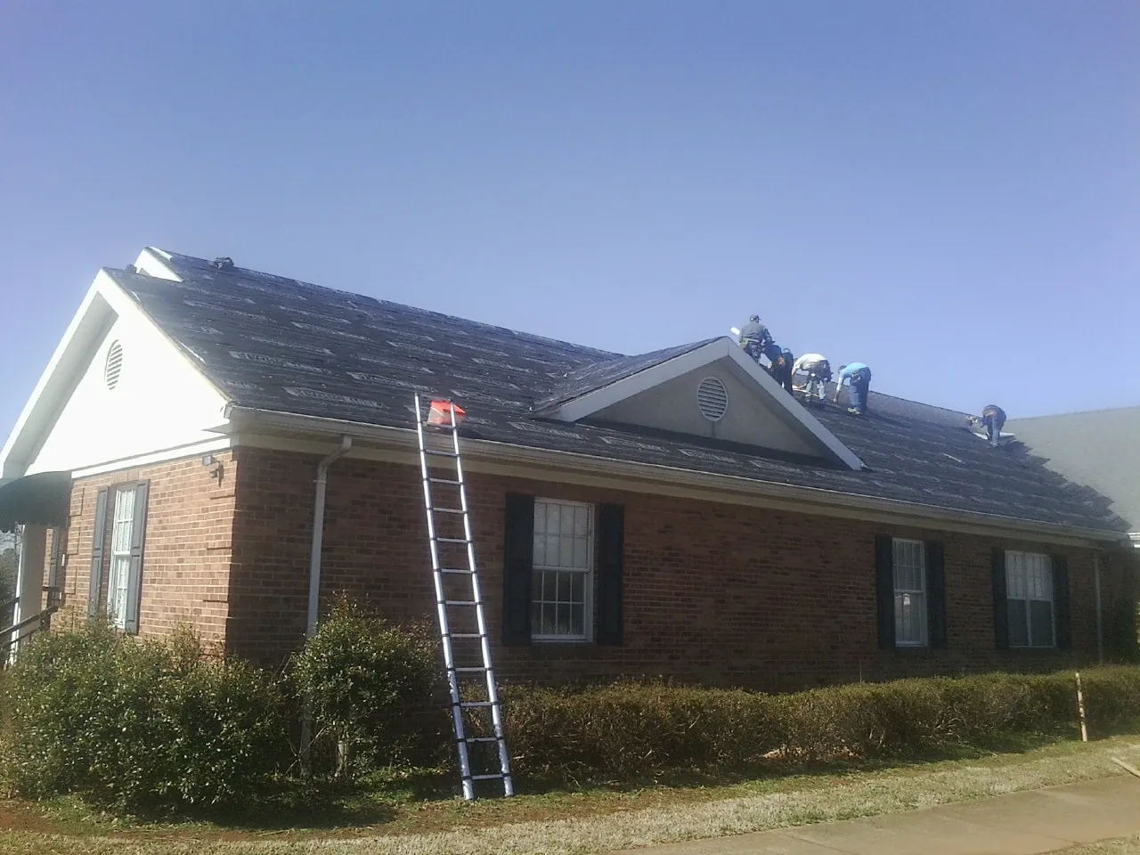 Crew tearing shingles off a brick ranch roof with a ladder set — Metal Roof Repair work by our crew in Mount Airy