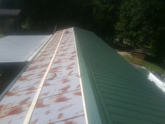 Old rusted panels beside newly installed green metal roofing — Wind Damage Roof Repair by Roofing Brothers in Mount Airy