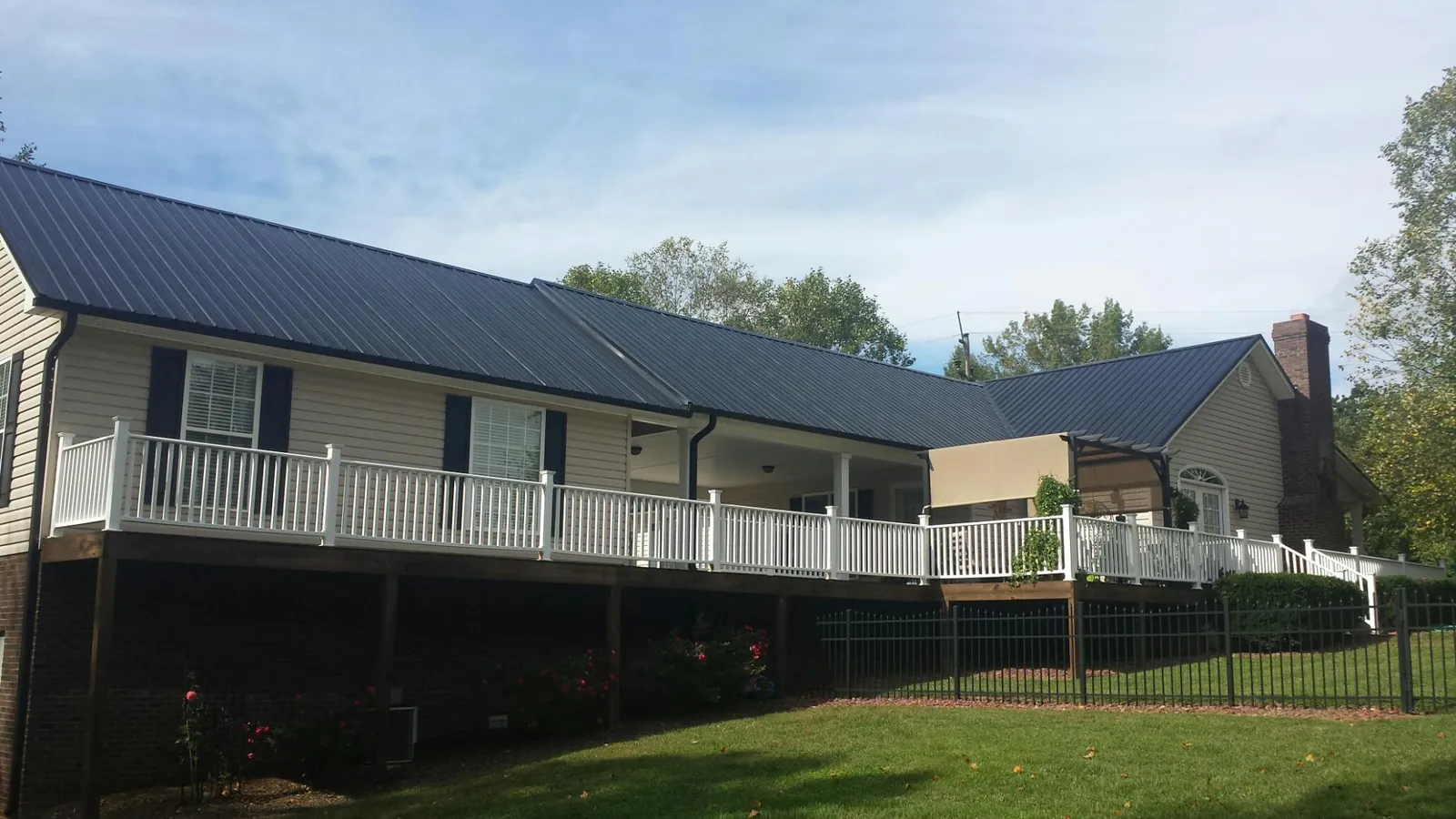 Black metal roof above a long white railed deck on a hillside home in Mount Airy
